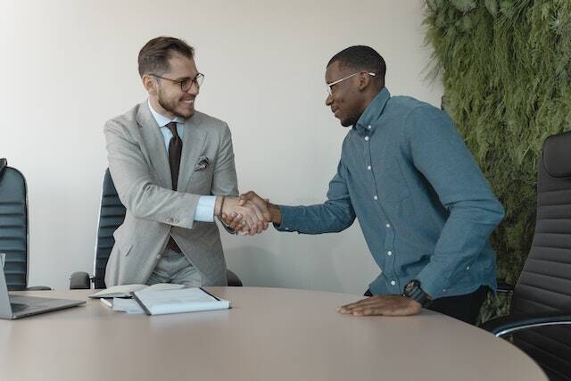 a person in a grey suit shaking hands with someone in a blue button down shirt